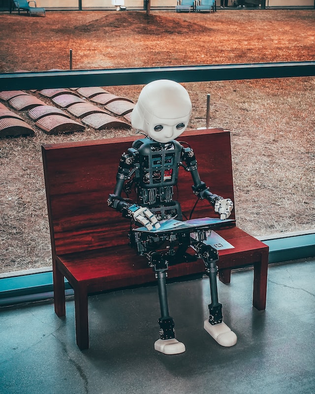 robot sitting on a bench using a laptop