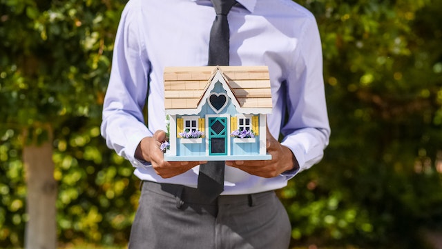 real estate agent in a suit holding a model of a house